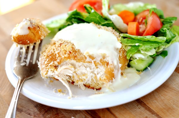 a white plate with chicken in a pillow, with a bite taken out , next to a green salad