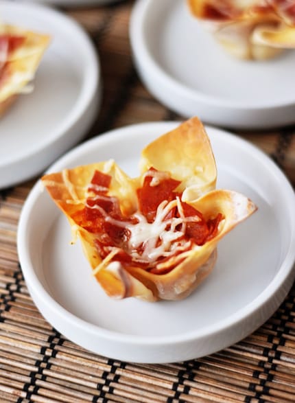 Small white plates with a small pizza appetizer cooked in a wonton wrap on each plate.