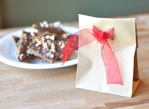 Paper sack with a red ribbon next to a plate of pecan buttercrunch toffee.