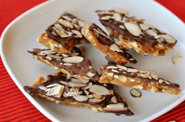 Pieces of almond roca stacked on their sides on a white plate.