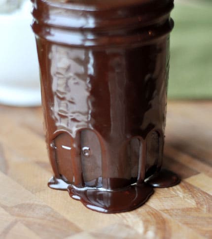 Jar filled with hot fudge sauce with some spilling over the sides.