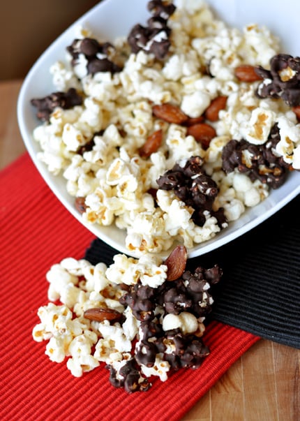 A white dish with kettle corn, partially chocolate-dipped and full almonds scattered throughout.