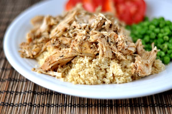 White plate with shredded pork, cooked couscous, peas, and sliced tomatoes.