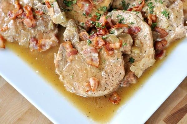 A white platter with smothered saucy cooked pork chops.