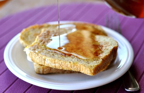 A plate of french toast with maple syrup being drizzled on it.