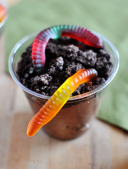 Top view of a clear plastic cup with chocolate pudding and crushed Oreo and a gummy worm on top.