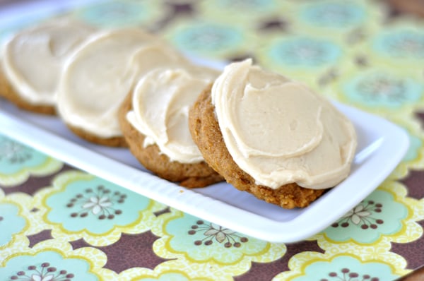 A white platter with four frosted pumpkin cookies.