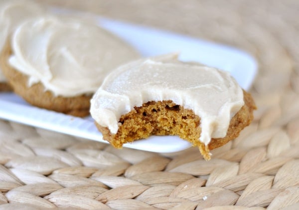 Frosted pumpkin cookie with a bite taken out on a white platter.