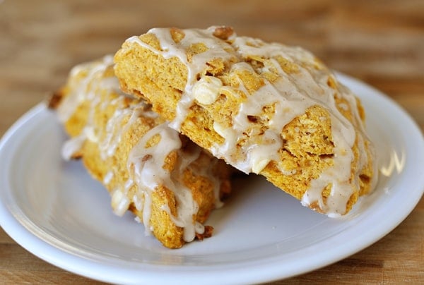 Two pumpkin scones drizzled with white icing on a white plate.