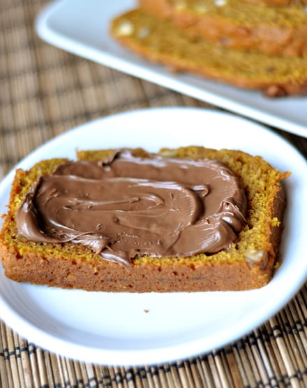 A slice of pumpkin bread with Nutella spread on it on a white plate.