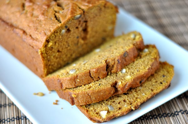 A loaf of pumpkin hazelnut bread with some slices cut on a white rectangular platter.