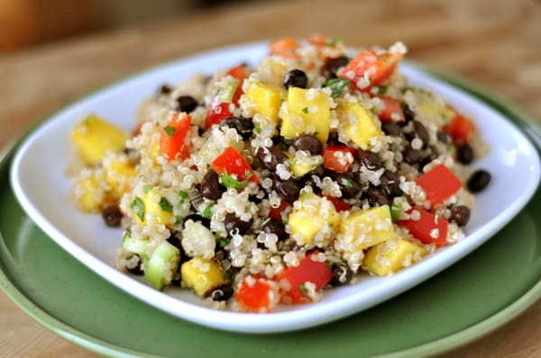 White plate with quinoa salad full of mangoes, tomatoes, cucumbers, and black beans.