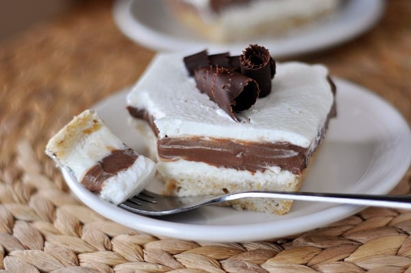 White plate with a piece of shortbread crust, pudding, and cool whip topped dessert with chocolate curls on top. 