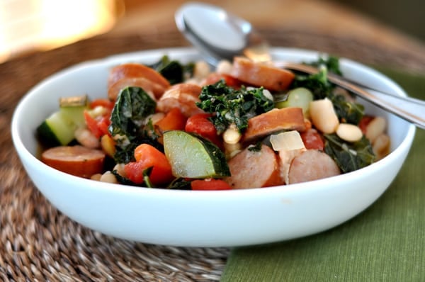 White oval bowl with sausage, kale, tomato, white bean, and zucchini ragout.