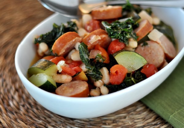 Top view of a white oval bowl filled with white bean and sausage ragout.