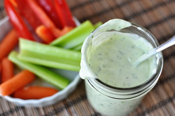 Top view of a glass mason jar of homemade ranch dressing and a white bowl of chopped vegetables.