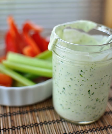 Glass mason jar full of homemade ranch dressing, with a bowl of fresh cut vegetables behind it.