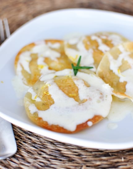 A white plate with four large ravioli drizzled with alfredo sauce.