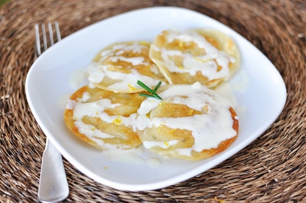 Top view of a white plate with four large cooked ravioli drizzled with a white sauce.