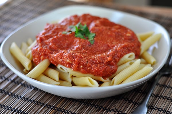 White bowl of cooked tube pasta smothered with red brie sauce.