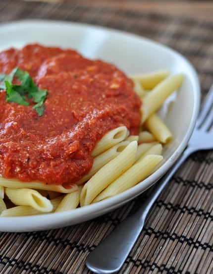 Cooked tube pasta covered with red sauce on a white plate.