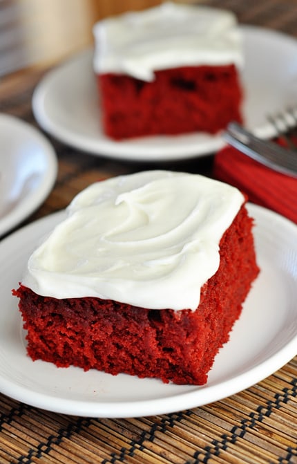 two pieces of red velvet cake with buttercream frosting on white plates