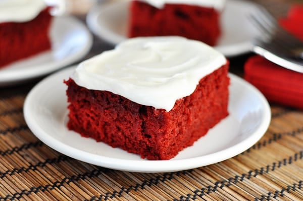 A piece of red velvet cake with cream cheese frosting on a white plate.