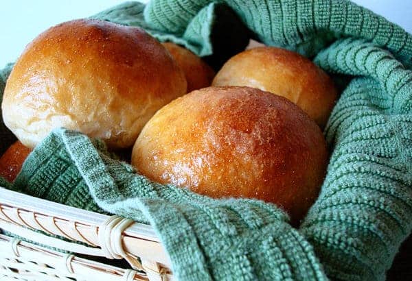 Golden brown rolls in a basket with a green towel.