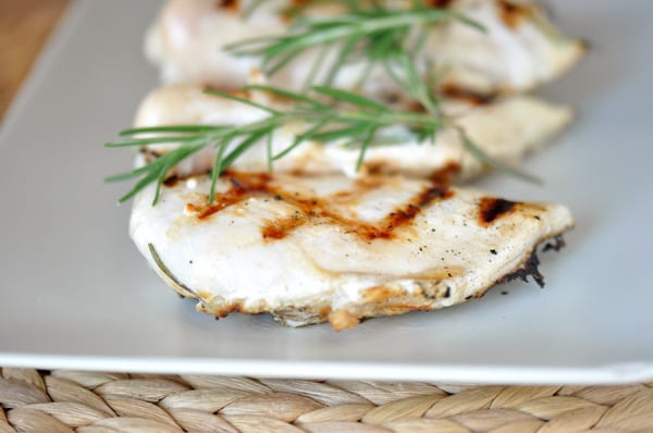 grilled chicken breasts on a white platter with sprigs of fresh rosemary on top