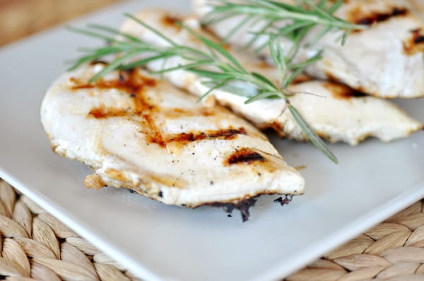 Grilled chicken breasts with rosemary springs on a white platter.