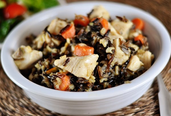 White bowl of cooked wild rice, carrot slices, and cubes of chicken.