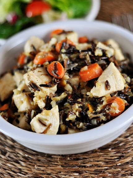 White bowl full of chicken cubes, cooked wild rice, and sliced carrots. 