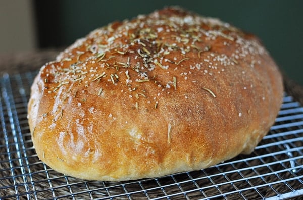 golden brown loaf of bread sprinkled with rosemary and salt on a cooling rack