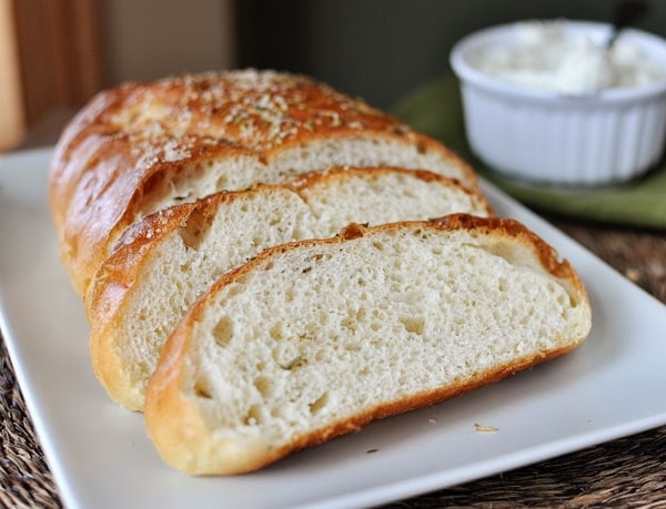 Half a loaf of rosemary bread with two big slices in front of the loaf, on a white rectangular plate.