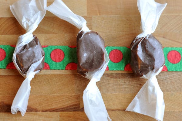 Three parchment wrapped chocolate caramels on top of a red and green ribbon.