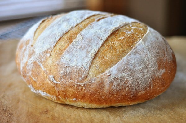 A loaf of freshly baked rustic crusty bread, dusted with flour, sitting on a cutting board. 