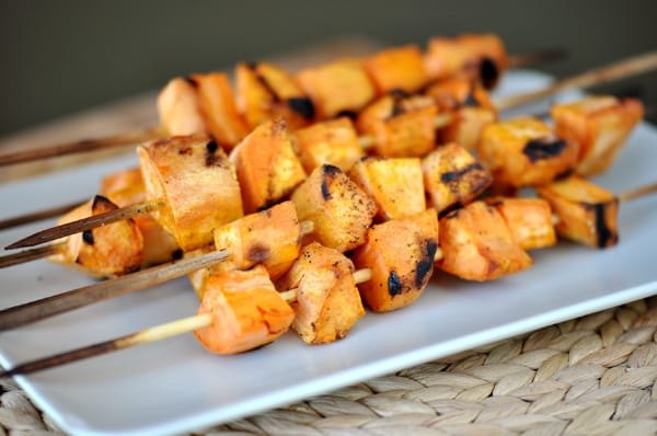 Side view of a white platter with grilled sweet potato skewers.