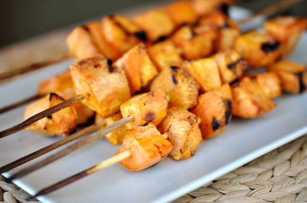 Rectangular white platter with grilled sweet potato skewers.