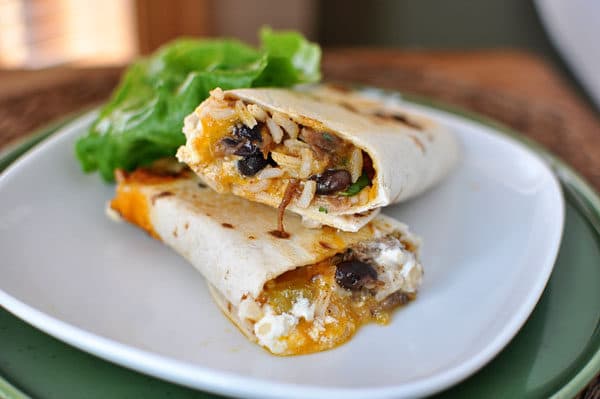 A griddled, rolled up tortilla sitting on a white plate, filled with southwest ingredients.