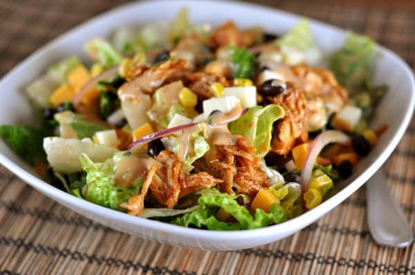 White bowl filled with salad, bbq chicken, corn, and slices of red onions.