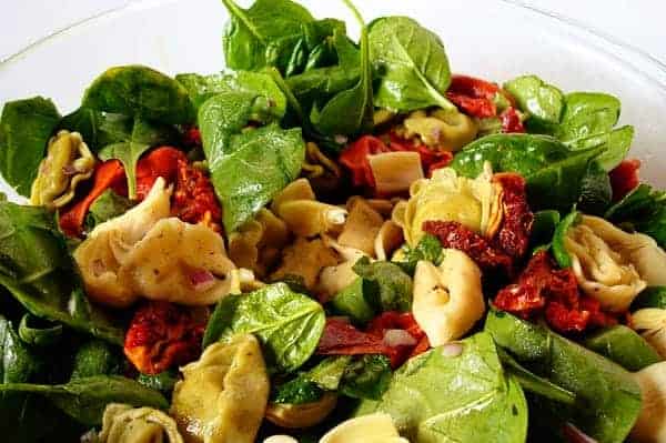 Spinach, tortellini, and sun-dried tomato salad on a white plate.