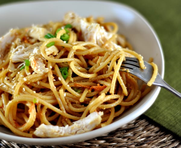 White dish with cooked pasta and chicken sprinkled with sesame seeds and green onions.