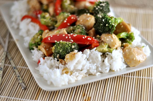 White rectangular platter with cooked white rice and sesame chicken and veggie stir-fry.