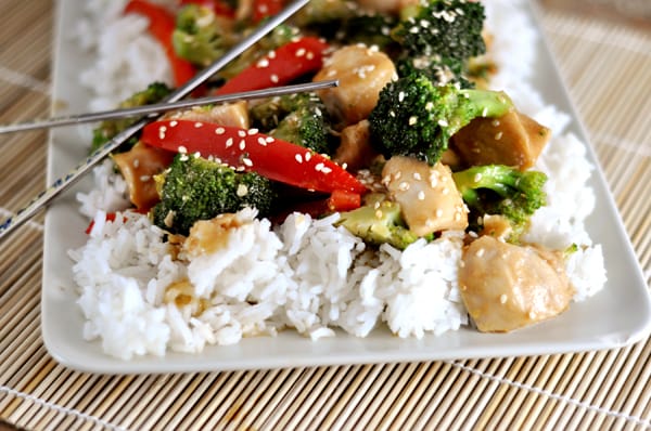 White platter with cooked white rice and sesame stir fry chicken.