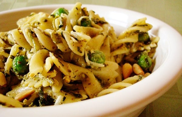 Pasta with pine nuts and peas in a white bowl.