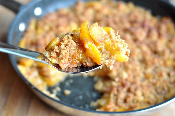 peach cobbler in a dark skillet with a scoop being taken out