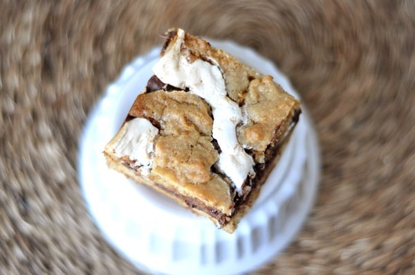 A cookie bar sitting on a white ramekin with ribbons of marshmallow and fudge inside the bar.