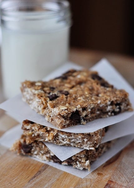 Squares of chocolate chip banana oat bars stacked on top of each other between squares of parchment paper.