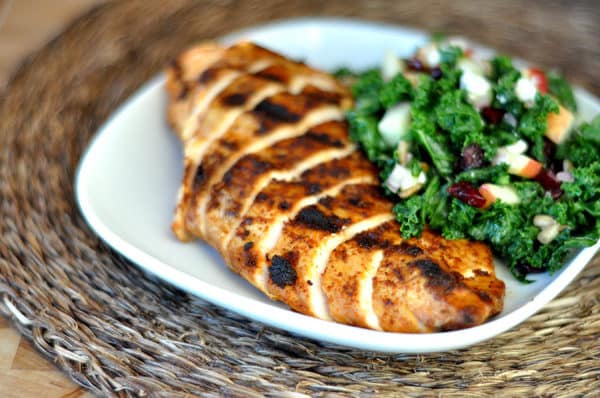 White plate with grilled sliced chicken breast next to a green salad.