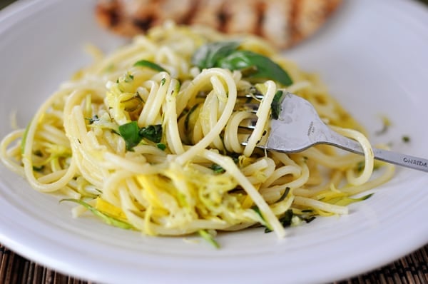 White plate with linguine pasta with cooked zucchini and yellow squash in it.